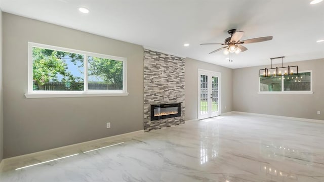 unfurnished living room featuring plenty of natural light, marble finish floor, ceiling fan, and a fireplace