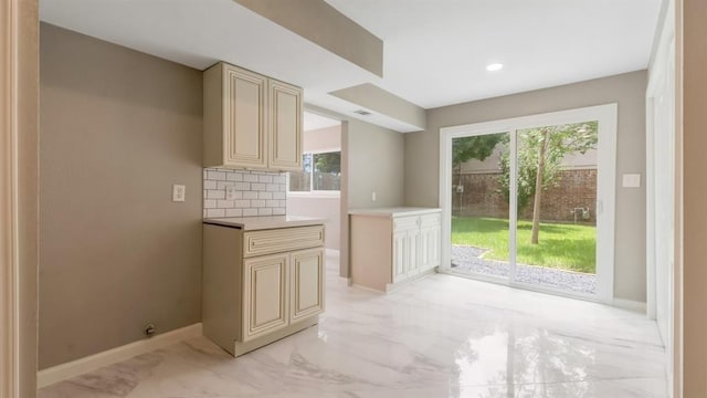 kitchen featuring light countertops, cream cabinetry, baseboards, marble finish floor, and backsplash