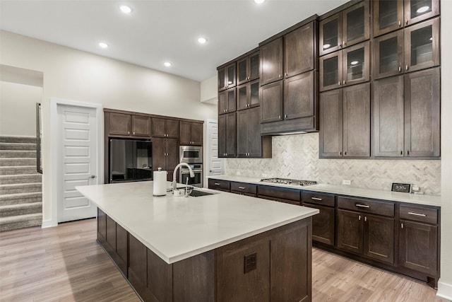 kitchen featuring stainless steel appliances, tasteful backsplash, light wood-type flooring, dark brown cabinets, and light countertops
