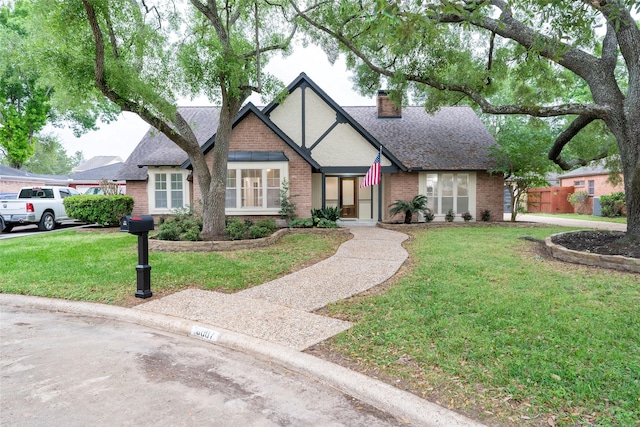 18007 Ravenfield Dr, Houston, TX 77084 - tudor house featuring a chimney, a shingled roof, brick siding, and a front yard