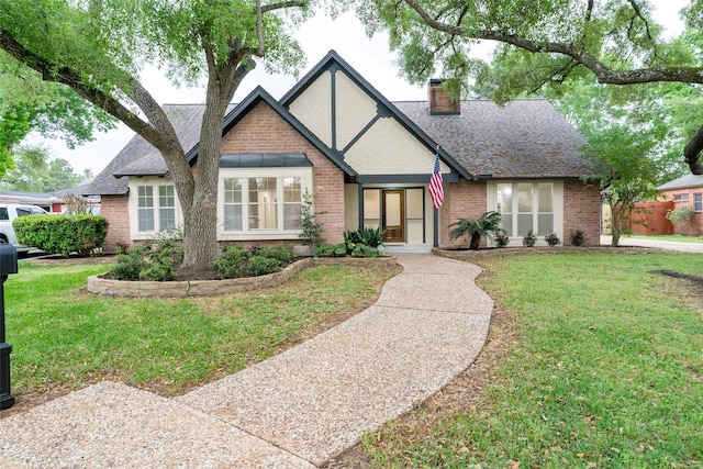 18007 Ravenfield Dr, Houston, TX 77084 - tudor-style house with brick siding, a front yard, a shingled roof, and a chimney