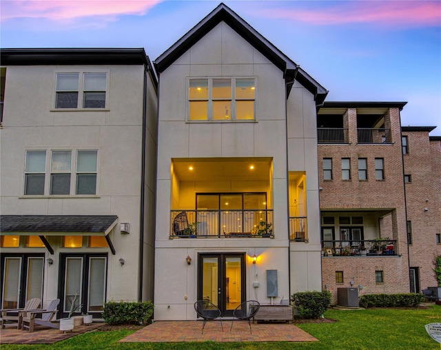 back of house at dusk featuring french doors, stucco siding, a yard, and a patio area