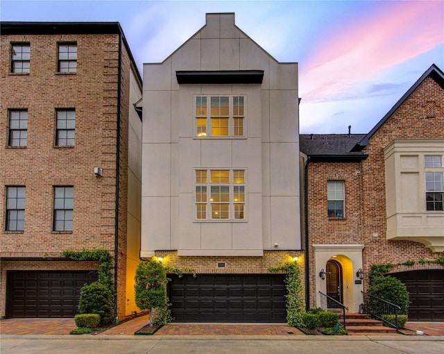 multi unit property with brick siding, decorative driveway, and an attached garage