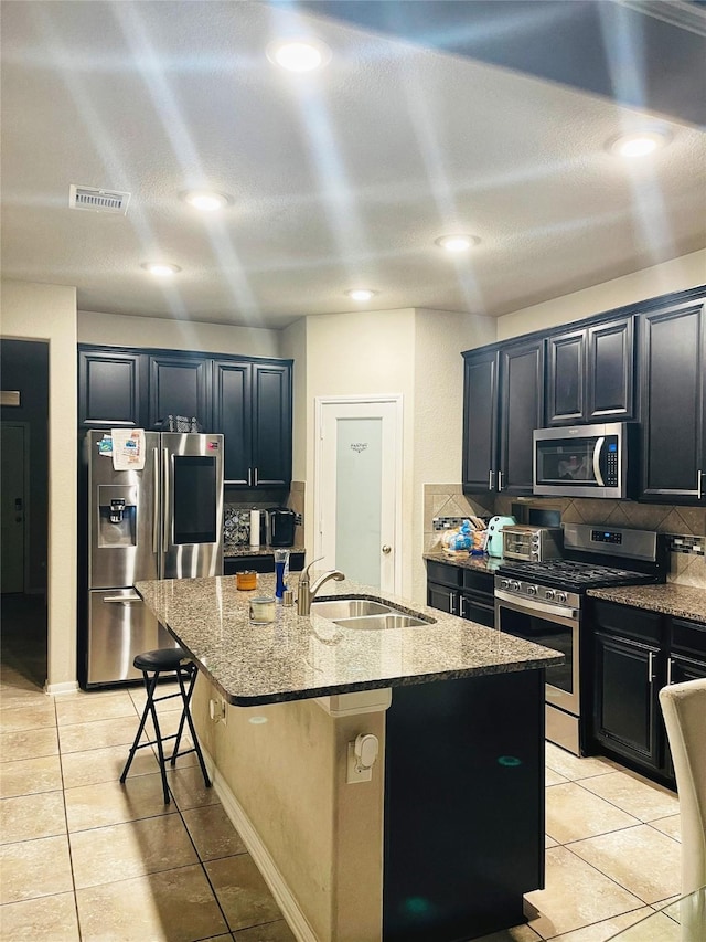 5114 Monarch Belle Ln, Katy, TX 77493 - kitchen featuring a sink, a kitchen island with sink, stainless steel appliances, light tile patterned flooring, and light stone counters