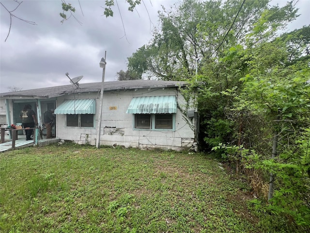 back of house featuring concrete block siding and a lawn