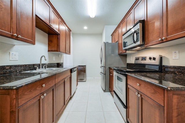 kitchen with light tile patterned floors, dark stone countertops, a sink, stainless steel appliances, and baseboards
