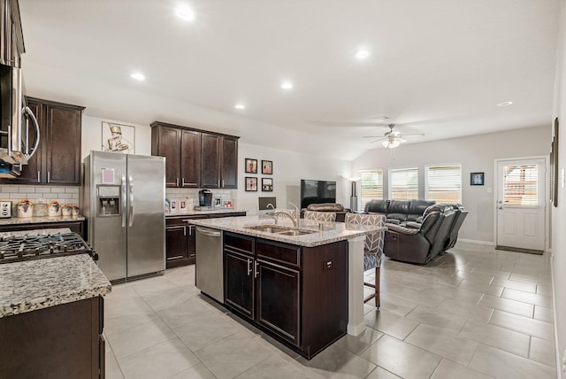 kitchen with a ceiling fan, a sink, open floor plan, stainless steel appliances, and backsplash