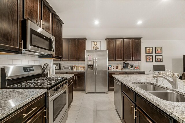 kitchen featuring a sink, dark brown cabinets, backsplash, light stone countertops, and appliances with stainless steel finishes