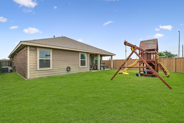 back of property with central air condition unit, a lawn, a fenced backyard, and a playground