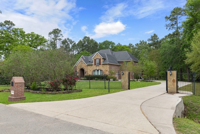 view of front of property featuring a gate, concrete driveway, brick siding, a fenced front yard, and a front lawn