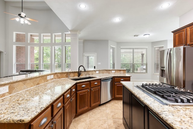 kitchen with stainless steel appliances, a ceiling fan, a sink, light stone counters, and light tile patterned floors