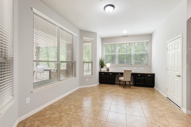 unfurnished office featuring baseboards, built in desk, and light tile patterned floors