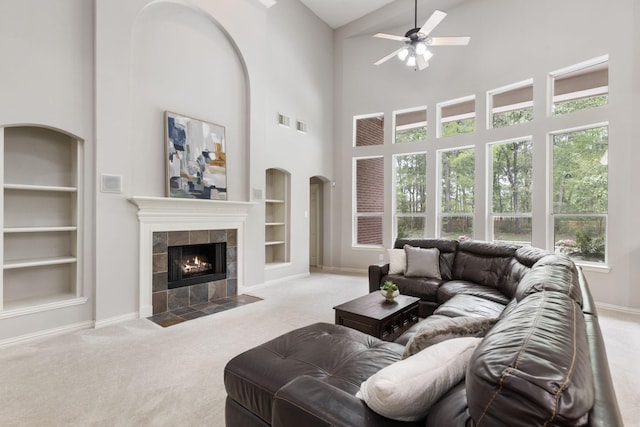 living room featuring carpet flooring, baseboards, a fireplace, a ceiling fan, and built in features