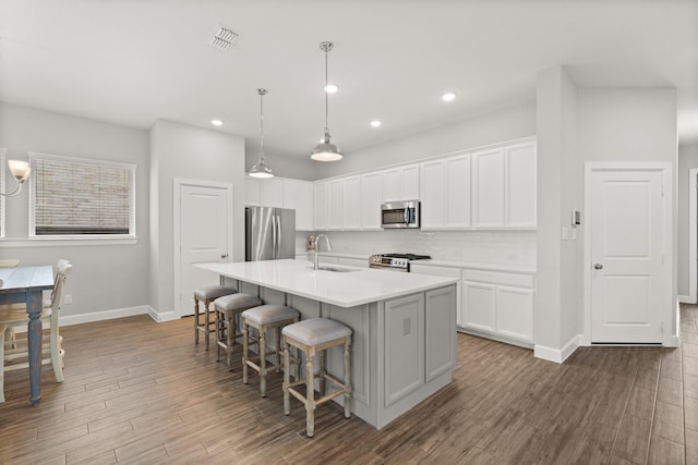 kitchen with an island with sink, a sink, baseboards, a kitchen bar, and appliances with stainless steel finishes