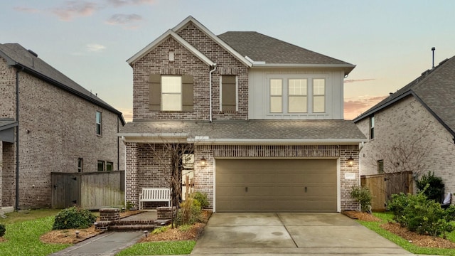 traditional home featuring concrete driveway, an attached garage, fence, brick siding, and roof with shingles