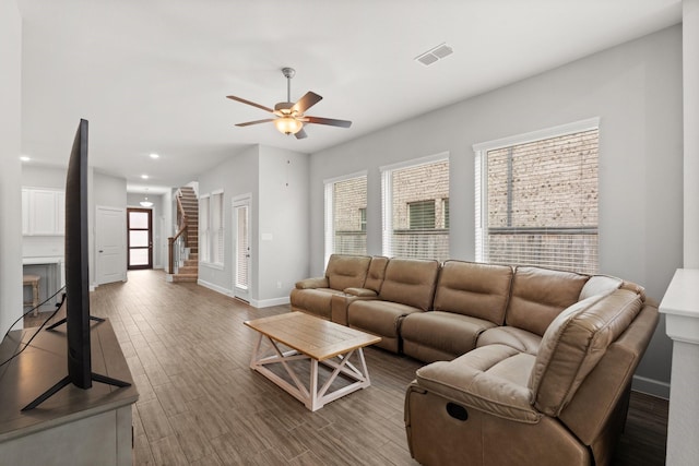 living room featuring a ceiling fan, wood finished floors, stairs, baseboards, and visible vents
