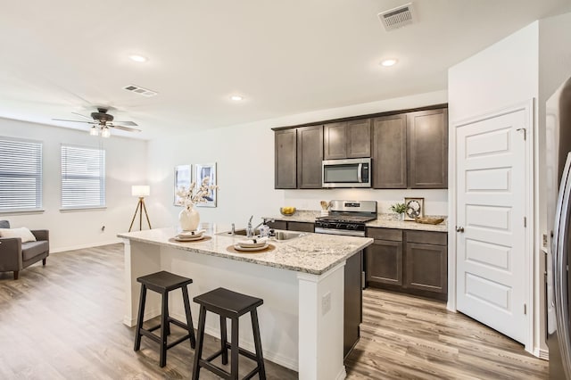 25617 Microstar Way, Montgomery, TX 77316 - kitchen featuring stainless steel appliances, a sink, dark brown cabinetry, a breakfast bar area, and light wood-style flooring