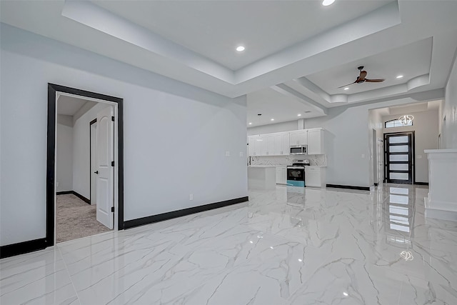unfurnished living room with baseboards, marble finish floor, a ceiling fan, and a raised ceiling