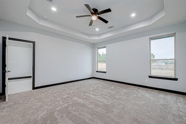 carpeted spare room with a tray ceiling, recessed lighting, baseboards, visible vents, and a ceiling fan