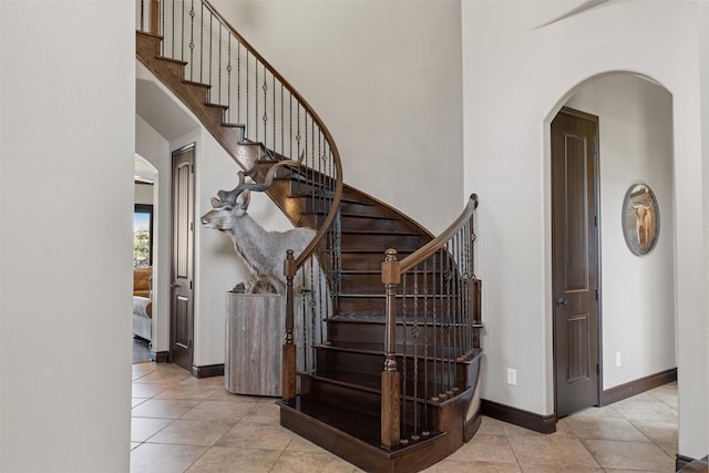 12606 Mostyn Ct, Magnolia, TX 77354 - stairway featuring tile patterned flooring, a towering ceiling, baseboards, and arched walkways