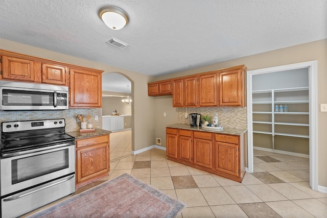 1231 Kings Creek Trl, Missouri City, TX 77459 - kitchen with light tile patterned floors, tasteful backsplash, arched walkways, visible vents, and stainless steel appliances