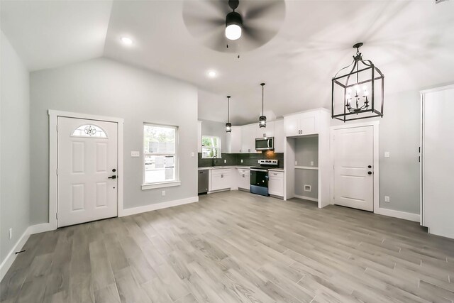 kitchen with appliances with stainless steel finishes, lofted ceiling, white cabinetry, light wood-style floors, and ceiling fan with notable chandelier