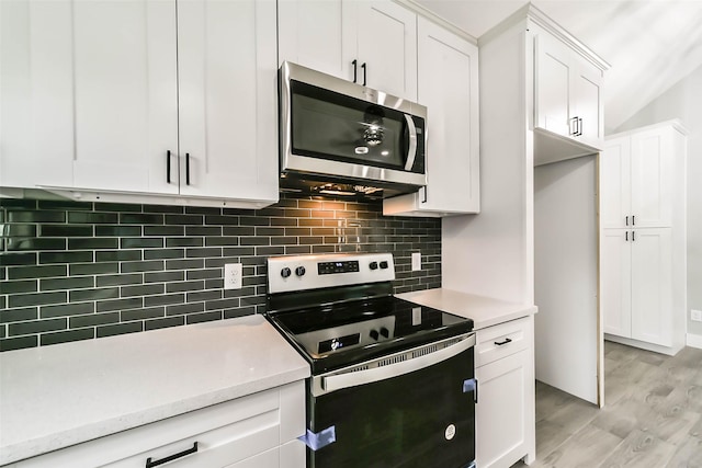 kitchen with light wood-style flooring, stainless steel microwave, white cabinetry, range with electric stovetop, and backsplash