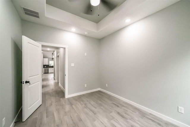 unfurnished room featuring a tray ceiling, baseboards, visible vents, light wood-style floors, and ceiling fan