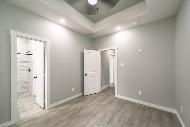 unfurnished bedroom with light wood-style flooring, baseboards, and a raised ceiling