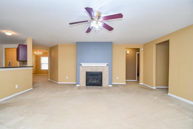 unfurnished living room with light colored carpet, baseboards, ceiling fan with notable chandelier, and a tile fireplace