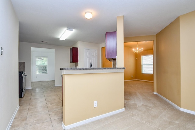 kitchen with a peninsula, baseboards, a notable chandelier, and black gas range