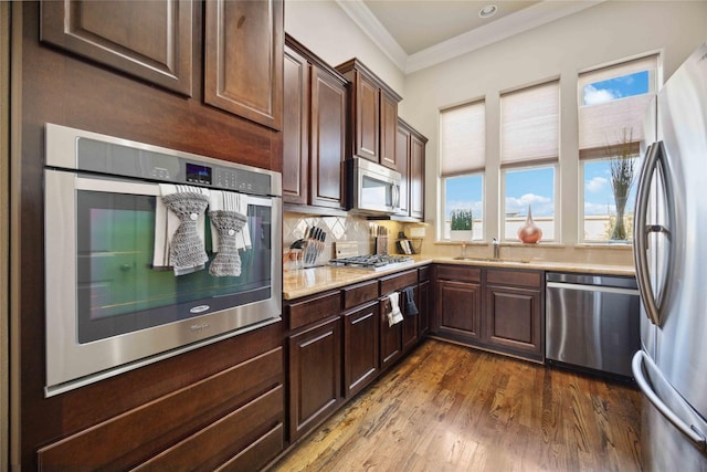 kitchen featuring crown molding, dark wood-style flooring, decorative backsplash, a sink, and appliances with stainless steel finishes