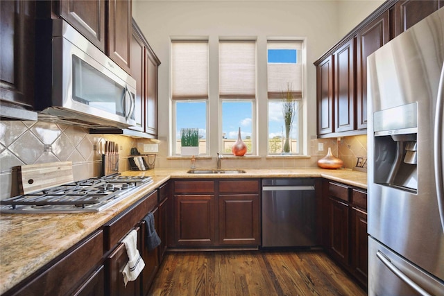 kitchen featuring tasteful backsplash, stainless steel appliances, dark wood-type flooring, a sink, and light stone counters