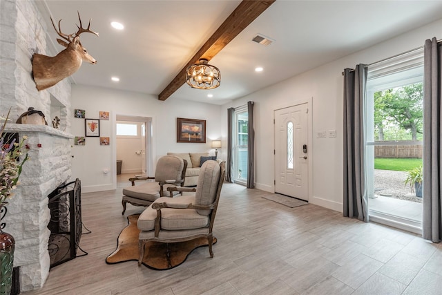 living room featuring visible vents, beam ceiling, an inviting chandelier, a fireplace, and wood finished floors