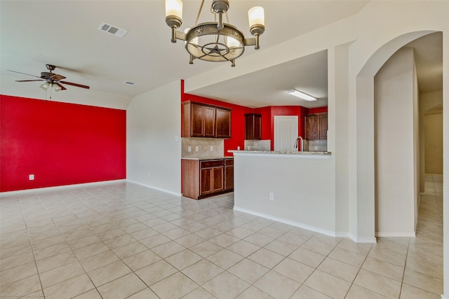 1056 Decker Dr, Fate, TX 75189 - unfurnished living room featuring ceiling fan with notable chandelier, an accent wall, light tile patterned flooring, arched walkways, and visible vents