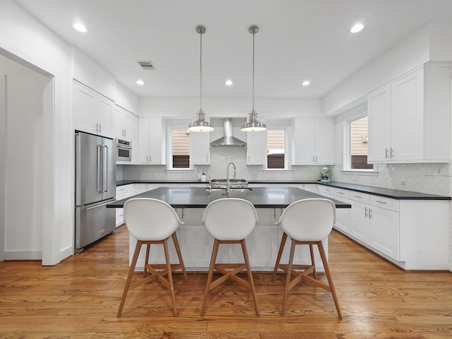 kitchen featuring a kitchen breakfast bar, high end fridge, dark countertops, wall chimney range hood, and visible vents