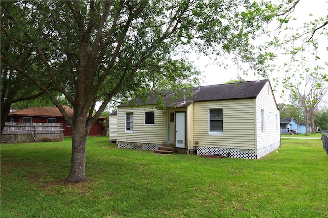 back of house featuring fence, entry steps, and a lawn