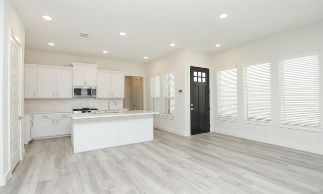 119 E 43rd St Unit A, Houston, TX 77018 - kitchen with stainless steel microwave, an island with sink, light countertops, white cabinets, and decorative backsplash