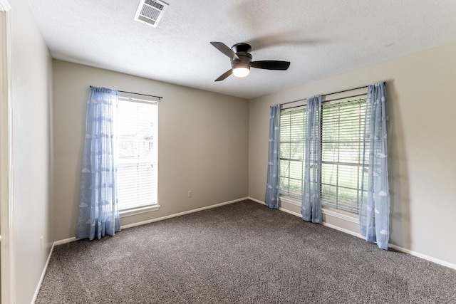 empty room featuring dark carpet, visible vents, a ceiling fan, and a healthy amount of sunlight