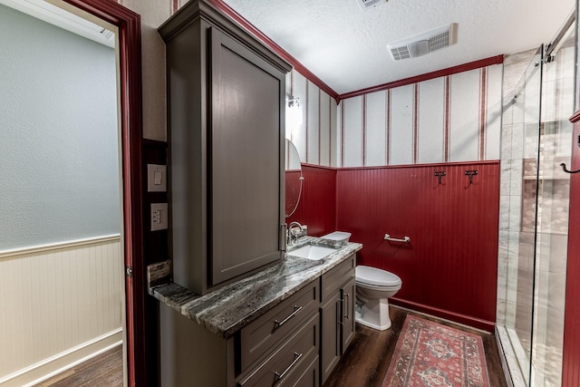bathroom featuring a textured ceiling, wood finished floors, wainscoting, and visible vents