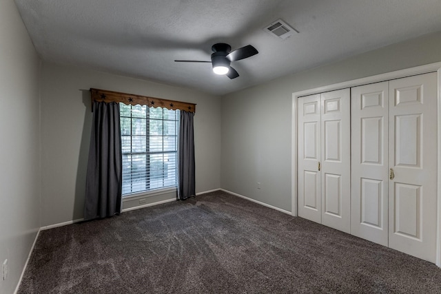 unfurnished bedroom with baseboards, a textured ceiling, a ceiling fan, visible vents, and dark carpet