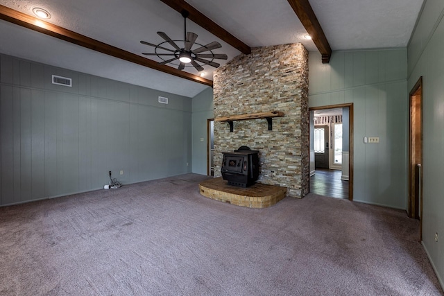 unfurnished living room with visible vents, a wood stove, a ceiling fan, beam ceiling, and carpet floors