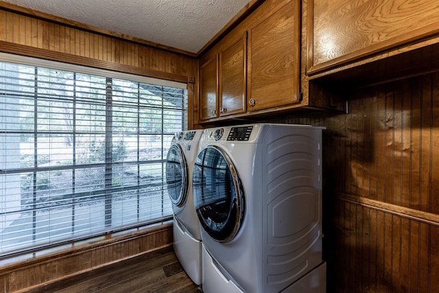clothes washing area featuring dark wood-type flooring, a textured ceiling, wood walls, cabinet space, and washer and clothes dryer