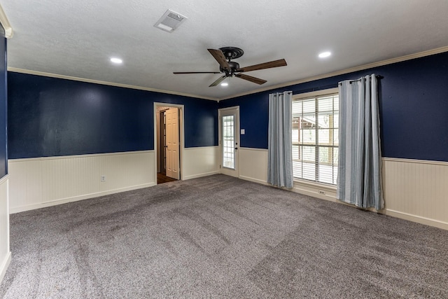 empty room with crown molding, a textured ceiling, a ceiling fan, visible vents, and wainscoting