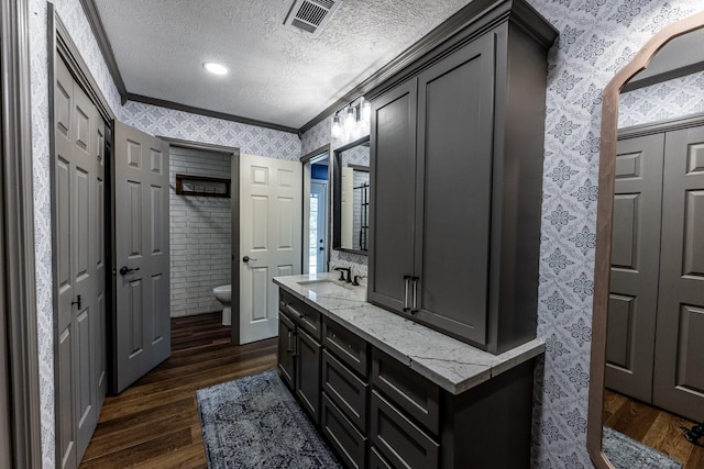 bathroom with crown molding, a textured ceiling, toilet, wood finished floors, and wallpapered walls