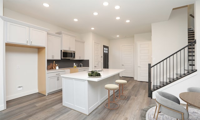 121 E 43rd St Unit B, Houston, TX 77018 - kitchen with white cabinets, stainless steel microwave, light wood-type flooring, and a center island with sink