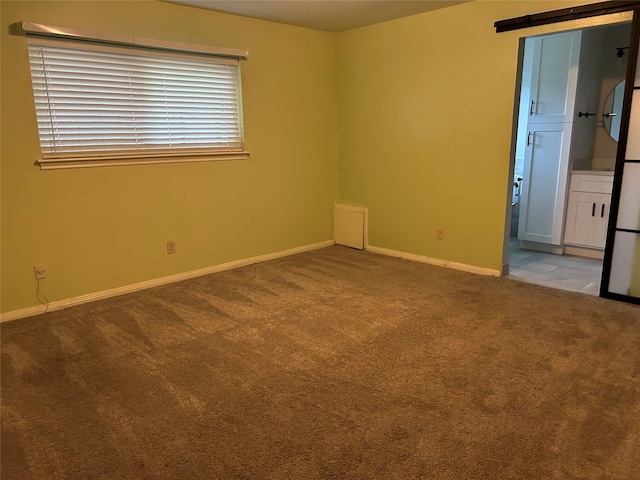 unfurnished room featuring a barn door, baseboards, and carpet