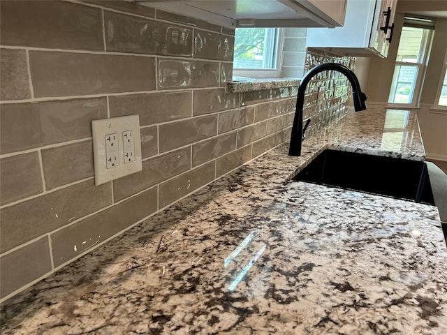 details featuring a sink, a fireplace, backsplash, and light stone counters