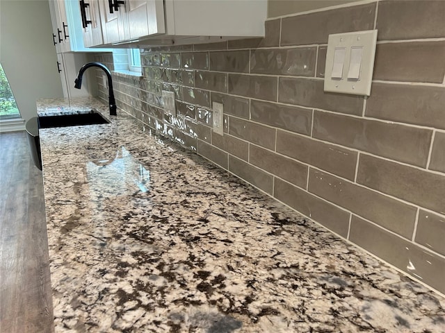 details featuring light stone countertops, a sink, white cabinetry, and decorative backsplash