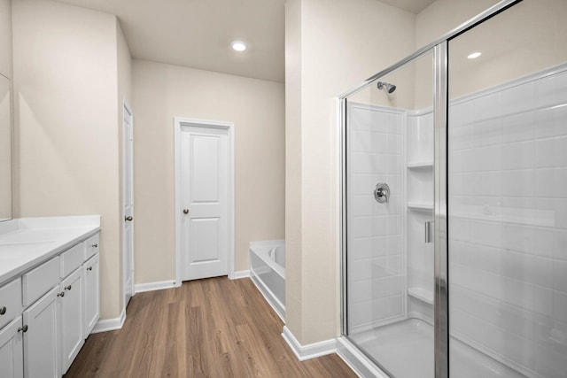 bathroom featuring a garden tub, wood finished floors, a stall shower, and vanity
